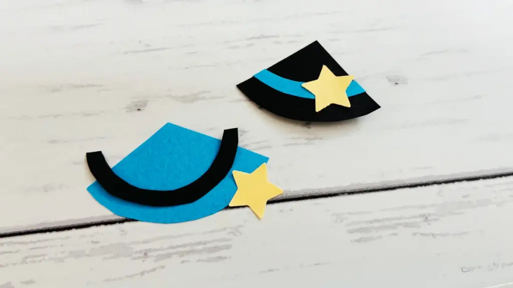 黒と青の画用紙で作った三角帽子のパーツに、星型を貼り付けて魔女帽子を製作している様子。