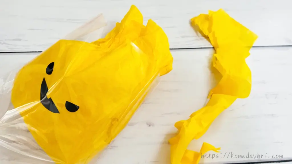 黄色いフラワーペーパーで包んだお菓子をラッピング袋に入れ、余った紙をカットして調整している様子。