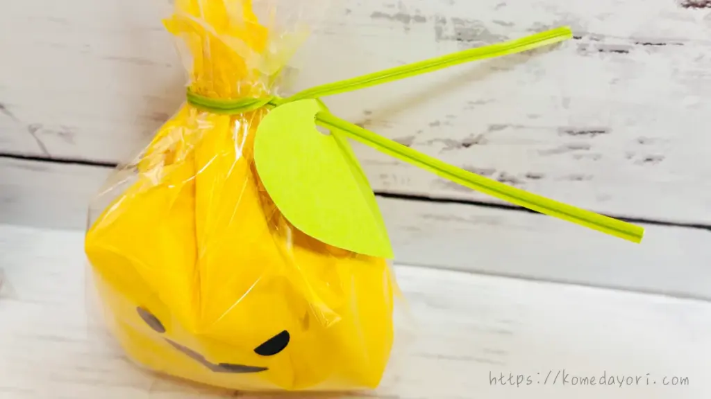 緑の画用紙で作った葉っぱを穴あけパンチで開け、タイに通して飾った黄色のかぼちゃラッピング。