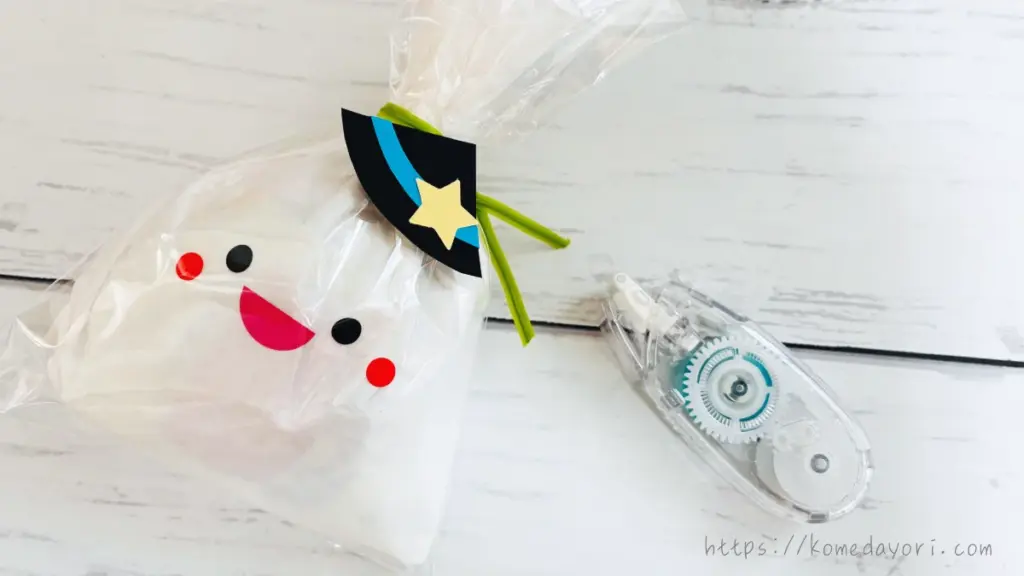 白いフラワーペーパーで包んだお菓子に顔をつけ、魔女帽子を飾ったおばけのハロウィンラッピング。横にテープのりが置かれている。
