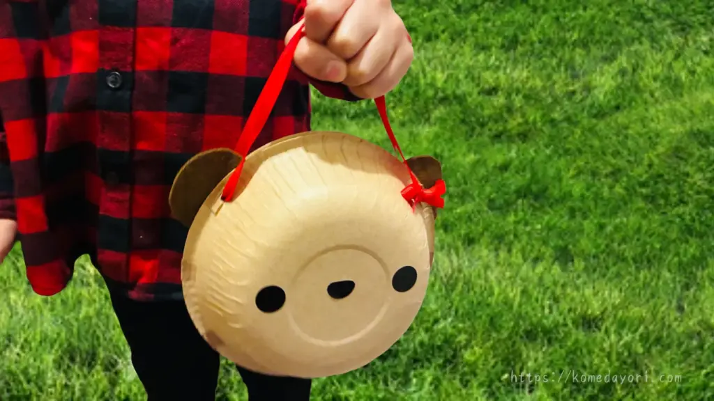 子どもが、紙ボウルで作ったくまのバッグを手に持っている様子。草の上で撮影している。