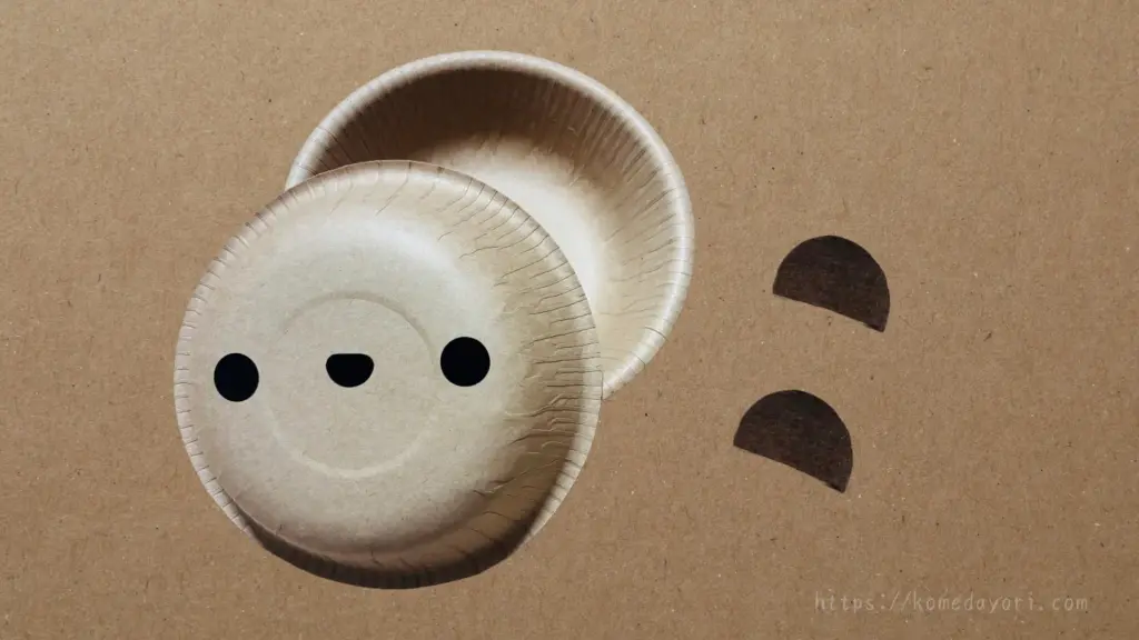 紙ボウル2枚と、黒い半円形の耳パーツ2枚を並べて置いている。紙ボウルにはポイントシールで作ったくまの顔つき。