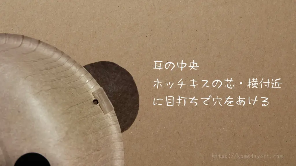 くま耳の位置に、目打ちで穴を開けている様子。「耳の中央 ホッチキスの芯・横付近に目打ちで穴をあける」という文字が入っている。