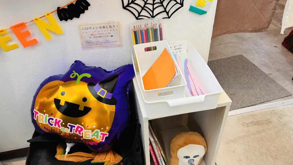 ハロウィン装飾がされた壁と、色鉛筆や紙が並んだ子ども向けの工作コーナーの写真。