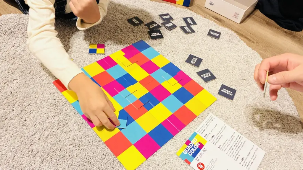 室内で家族がカラフルなボードゲーム”QUADRO COLOR”を楽しんでいる様子。子どもの手が写っている。