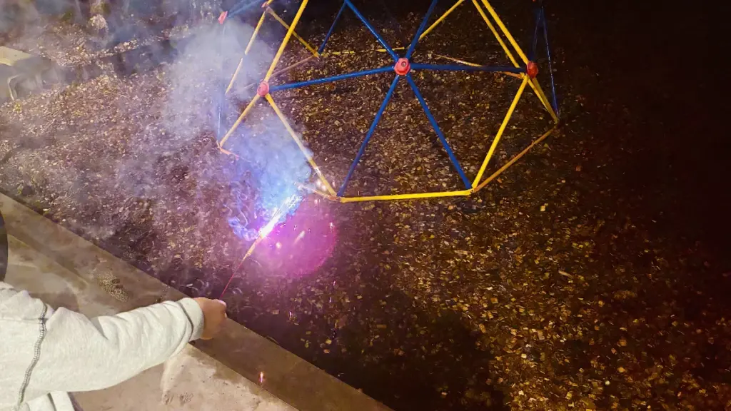 夜の屋外で手持ち花火を楽しむ様子。子どもの手と花火の光が写っている。