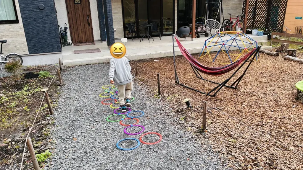 子どもが宿の庭でケンケンパリング遊びに夢中になっている様子。ハンモックやジャングルジムもある子ども向けの遊び場。