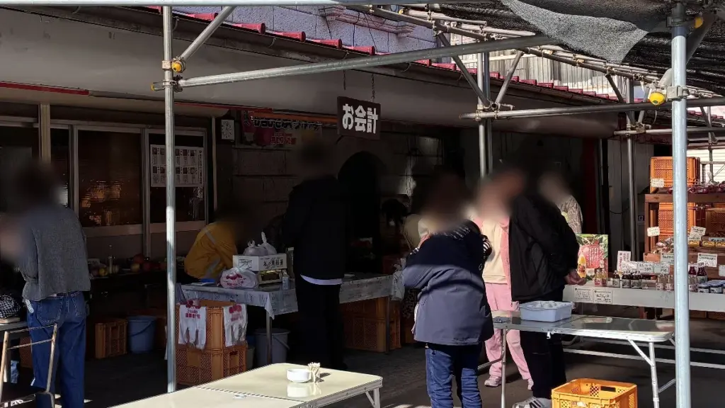 荒巻りんご園の直売所のお会計スペース。複数の来園者が並び、販売商品が並ぶ屋台風のスペース
