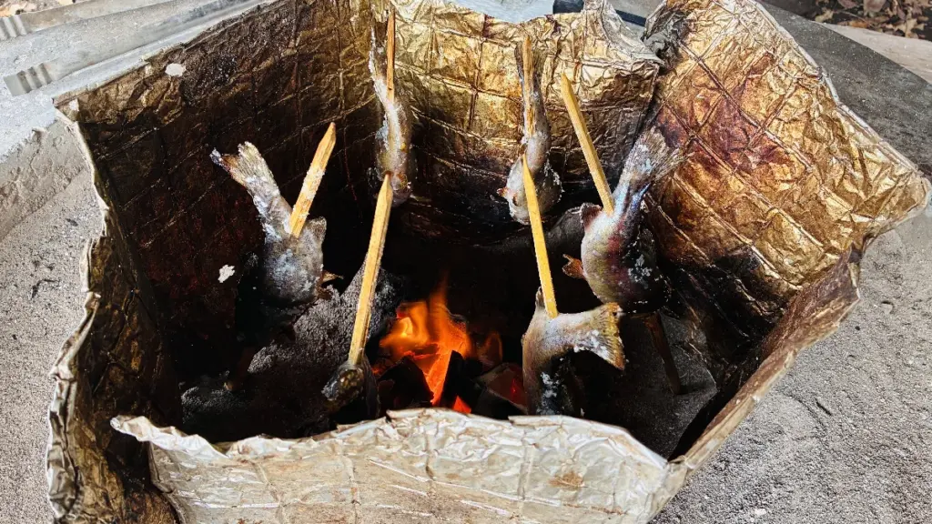 囲炉裏の強い火でニジマスが焼かれているアップ写真。炎と串の魚がよく見える。