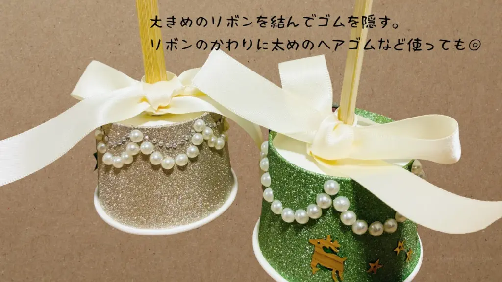 完成したハンドベル2個(ゴールドとグリーン)が並んでいる様子。大きめのリボンを結んでゴムを隠す。リボンのかわりに太めのヘアゴムなど使ってもOKと記載されている。