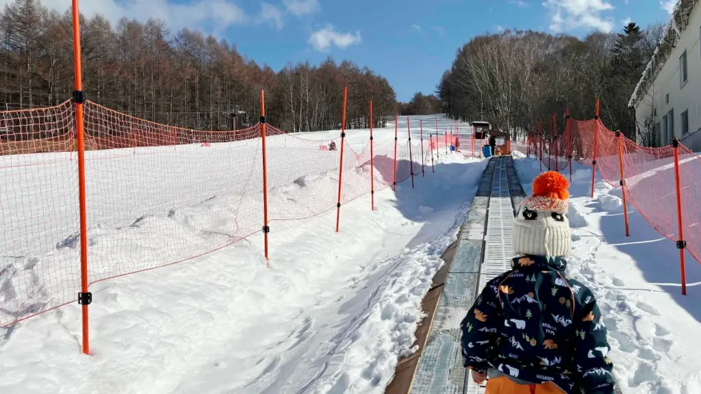 スノーエスカレーターに乗って雪山の斜面を登る子供の後ろ姿。周囲は安全ネットで囲まれている。
