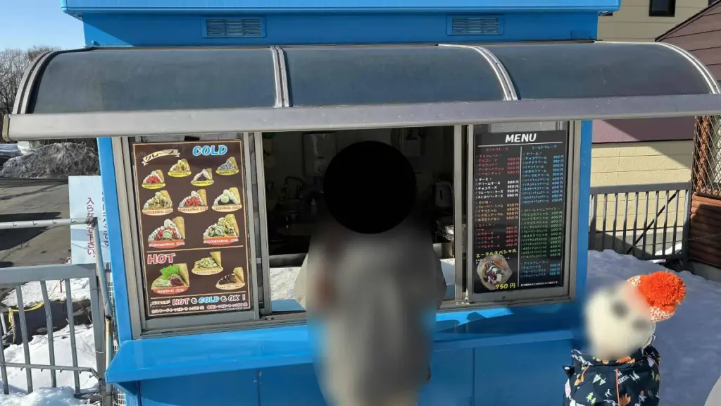 青い外観のマリオンクレープの売店。店頭には種類豊富なクレープメニューが掲示されている。