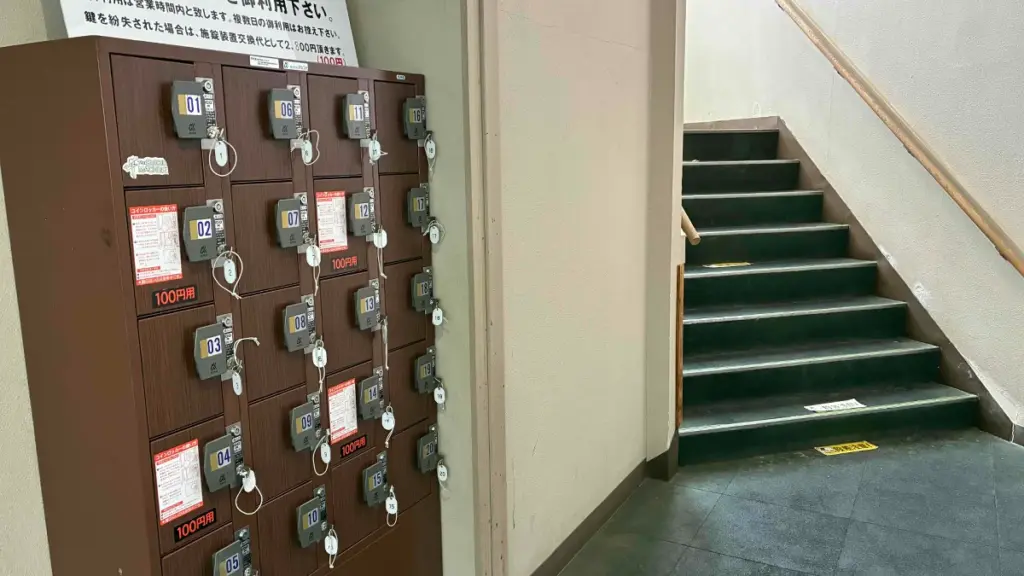建物内の階段横に設置された茶色のコインロッカー。100円硬貨専用で、利用上の注意書きが貼られている。