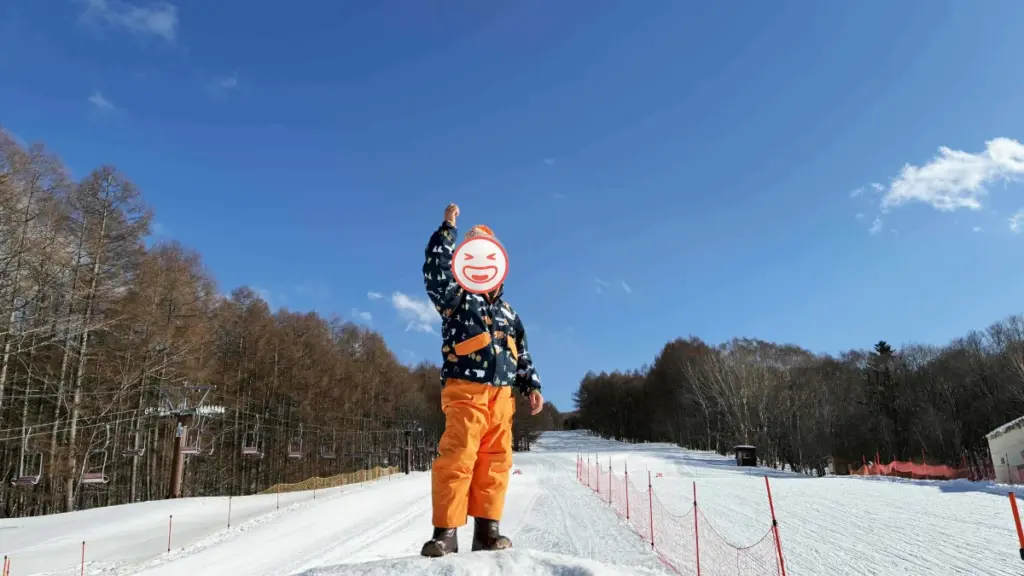 晴天のゲレンデで、雪山をバックにガッツポーズをして喜ぶ子供の全身ショット。