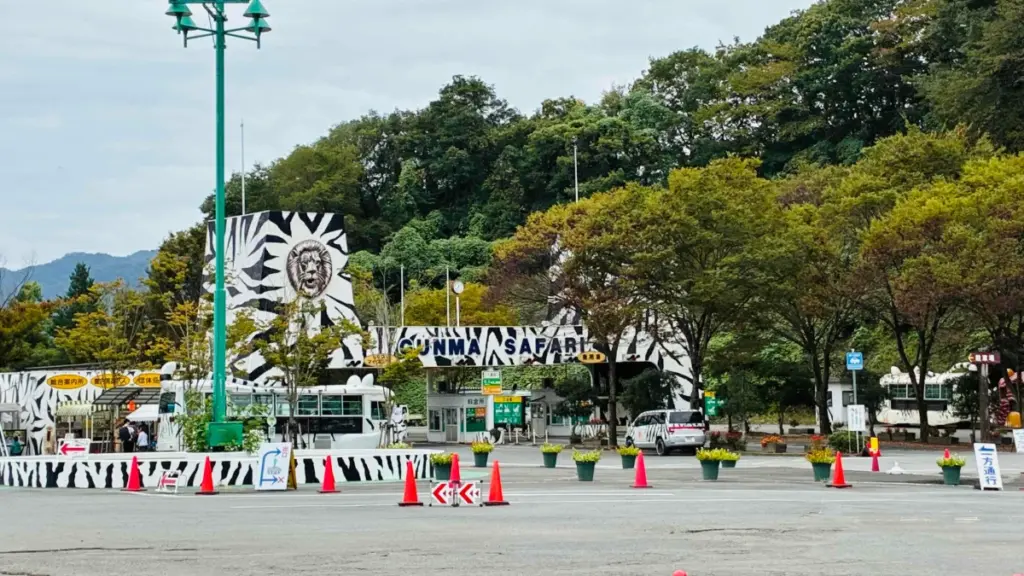 群馬サファリパークの入口全景。ゼブラ柄の建物とライオンのモチーフが目を引き、料金所や総合案内所が並ぶ広々とした敷地が広がっている。