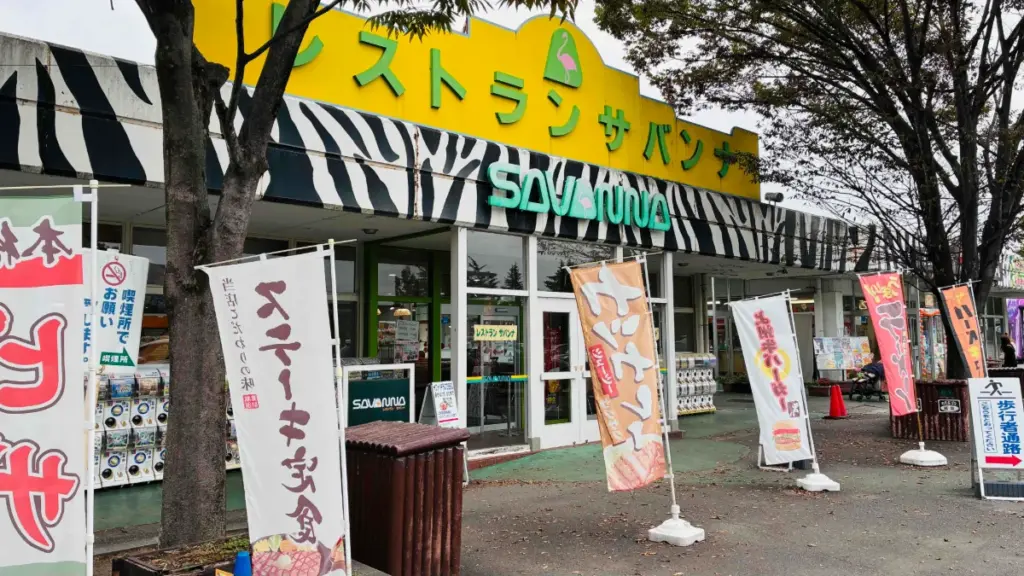 群馬サファリパーク内のレストラン「サバンナ」の外観。黄色い看板とシマウマ柄の装飾が目立ち、入口前にのぼり旗が並んでいる。