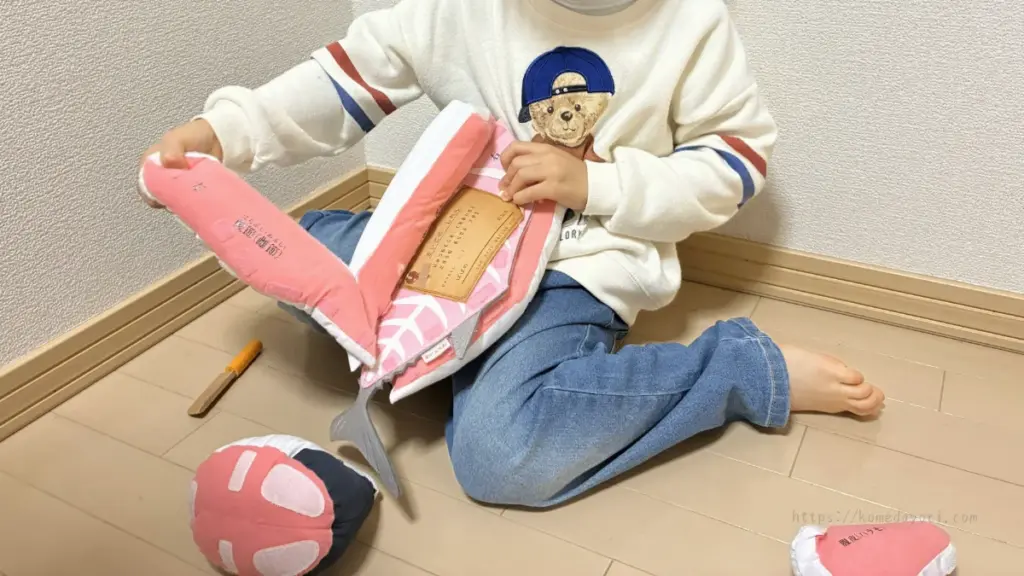 子どもが大きな魚のぬいぐるみから試練カードを確認している様子。