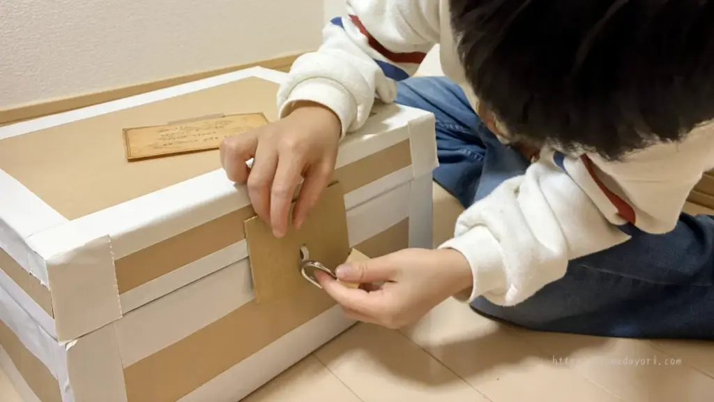 子どもが手作り宝箱にかかっている南京錠を開けようとしている瞬間。