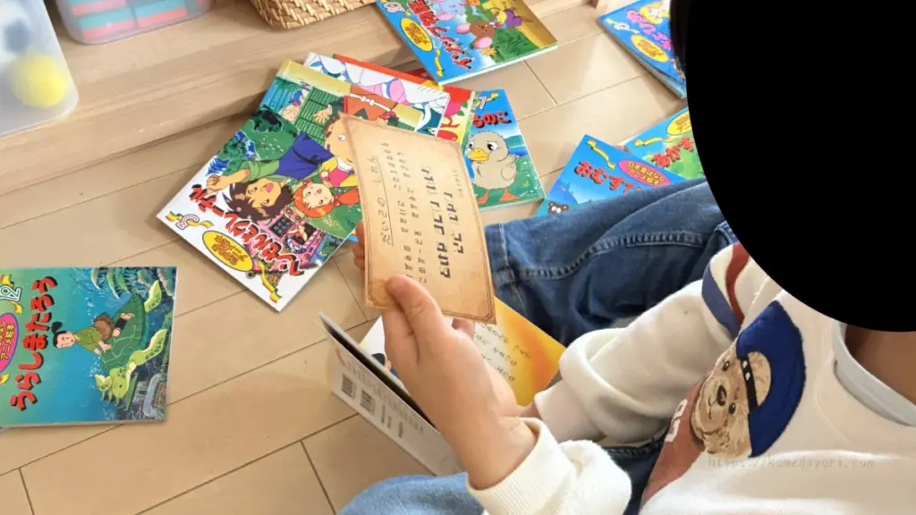 子どもが床に座り、複数の絵本やカードを広げて試練カードを確認している様子。