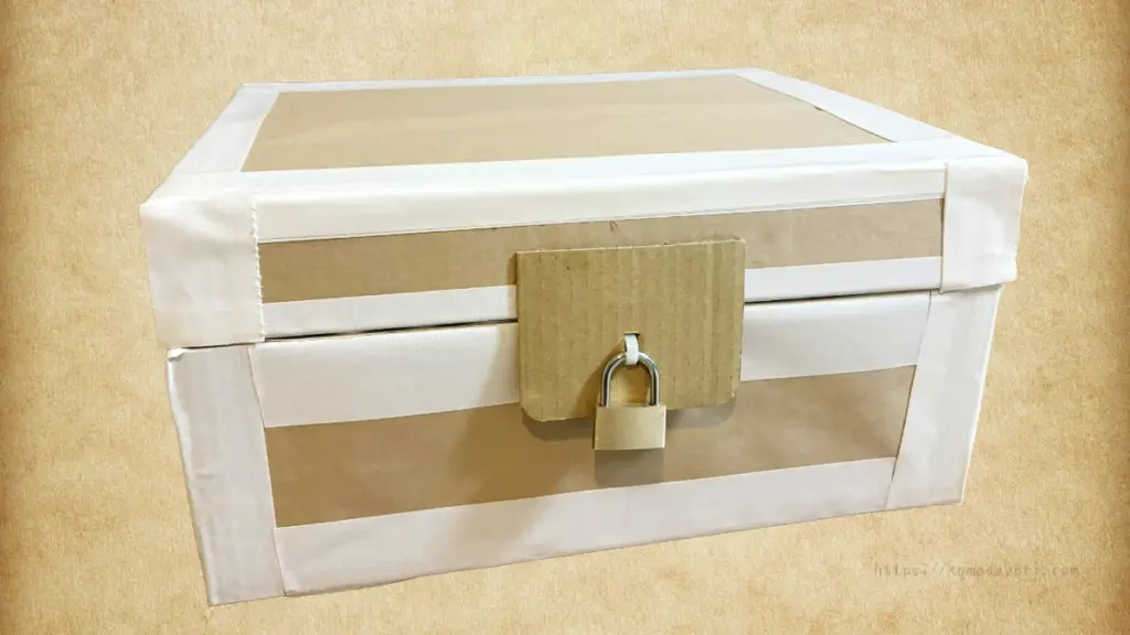 段ボール箱で作られた宝箱の完成形。白いガムテープで補強され、茶色の蓋が付いており、中央に黄色の南京錠が取り付けられている。
