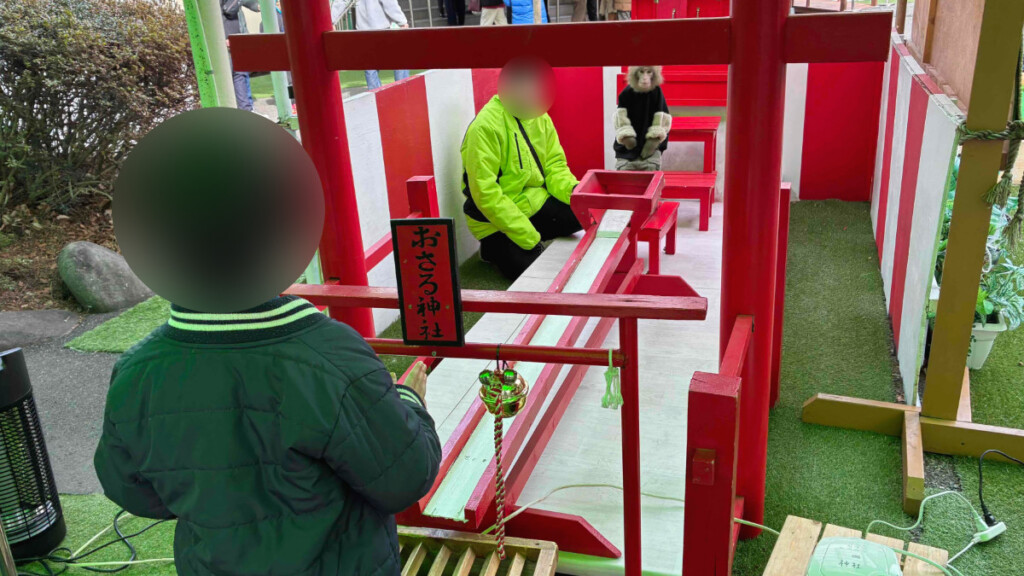 おさるランドの「おさる神社」猿がおみくじ入りのボールを子供に渡す様子。(人物はぼかし加工)。