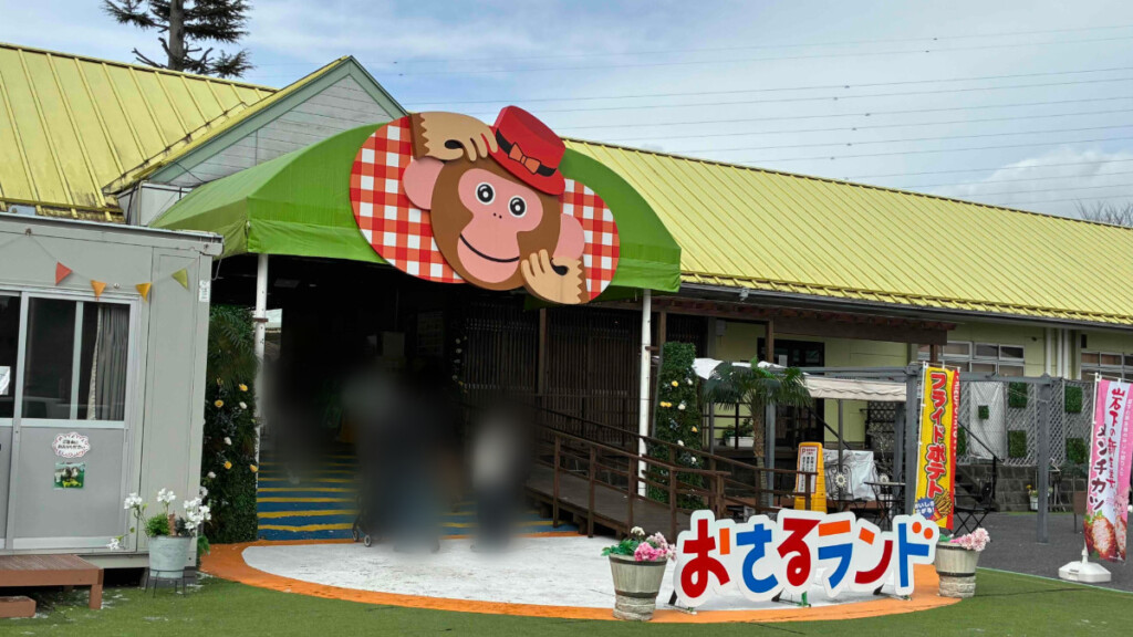 日光さる軍団「おさるランド」の入り口。黄色い屋根とサルを模した大きな看板、複数の人物が写っている(ぼかし加工あり)。