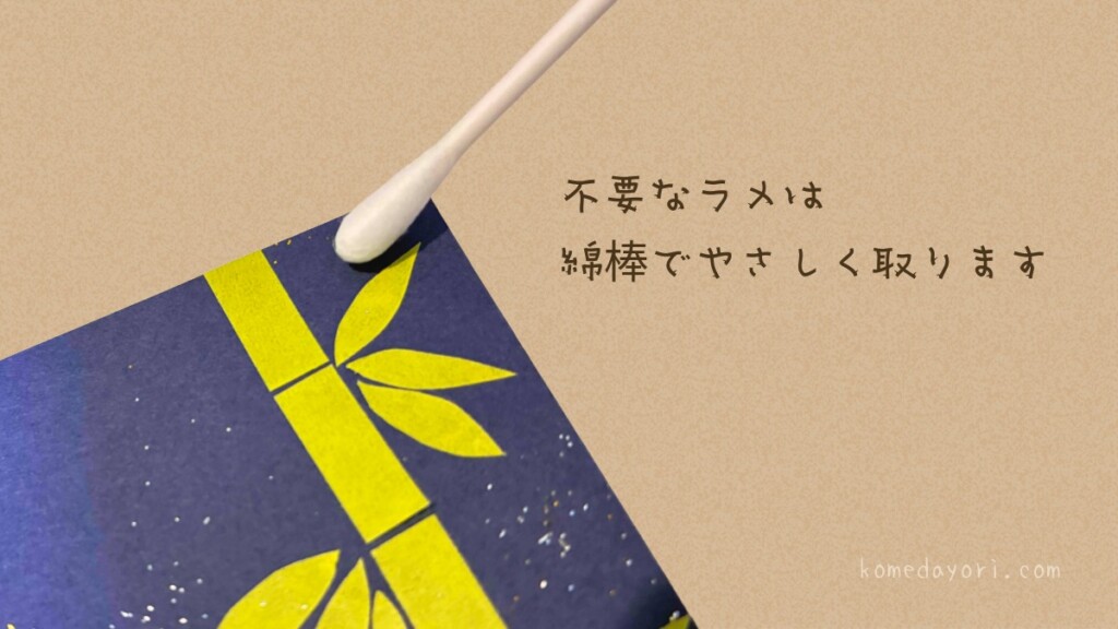 画用紙の端についた余分なラメパウダーを、綿棒を使って優しく拭き取っている様子。画面に「不要なラメは綿棒でやさしく取ります」の文字あり